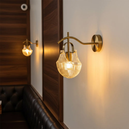 Luxury gold wall sconce light fixture with a textured glass shade casting a warm glow over a restaurant booth seat.