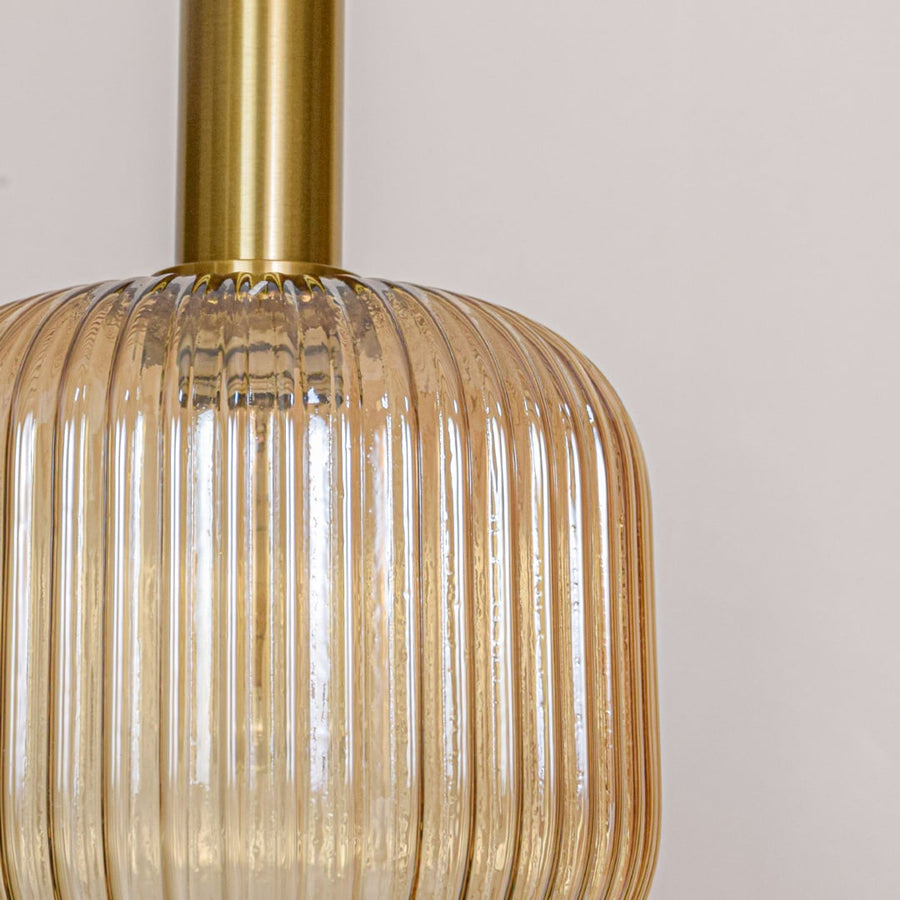 Closeup of amber ribbed glass pendant light showing vertical texture gold metal top and premium decorative lighting finish.