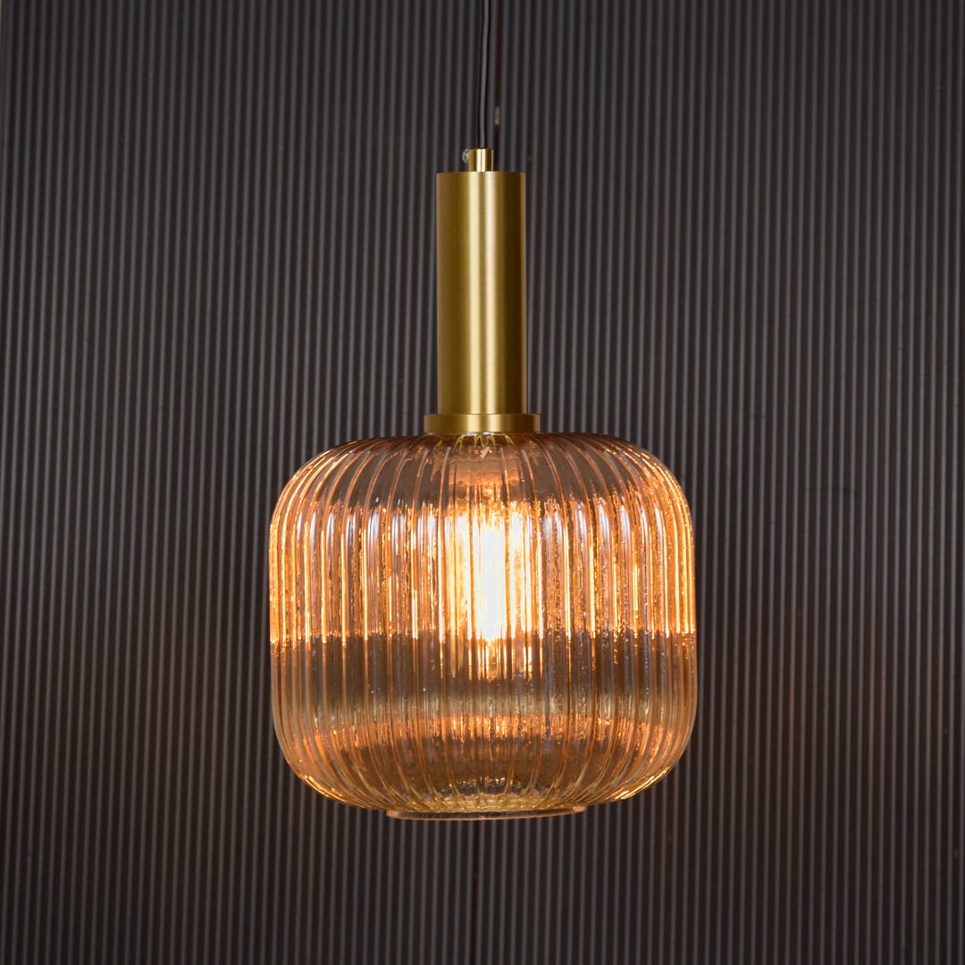 Gold metal and ribbed glass pendant light switched on against black background delivering soft warm ceiling lighting effect.