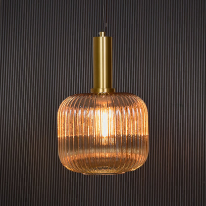 Gold metal and ribbed glass pendant light switched on against black background delivering soft warm ceiling lighting effect.