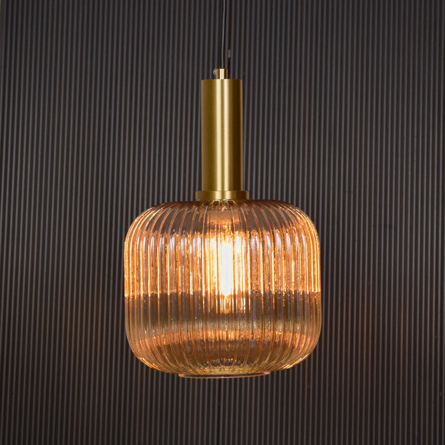 Gold metal and ribbed glass pendant light switched on against black background delivering soft warm ceiling lighting effect.