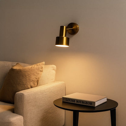 A warm modern living room with a gold wall lamp glowing softly above a beige sofa creating a cozy ambient light effect against a calm neutral wall.