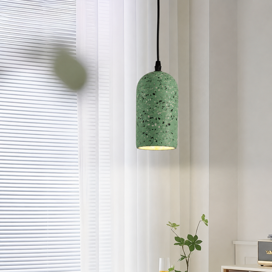 A green speckled pendant light with a terrazzo-style finish hangs in a bright room with white blinds and a small plant below.