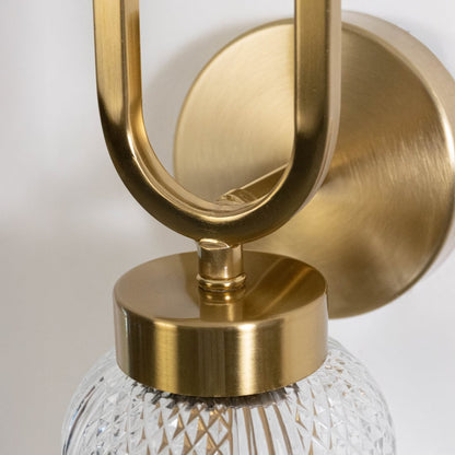 Closeup of luxury gold wall sconce with oval loop design and textured glass shade showing detailed craftsmanship and premium style.
