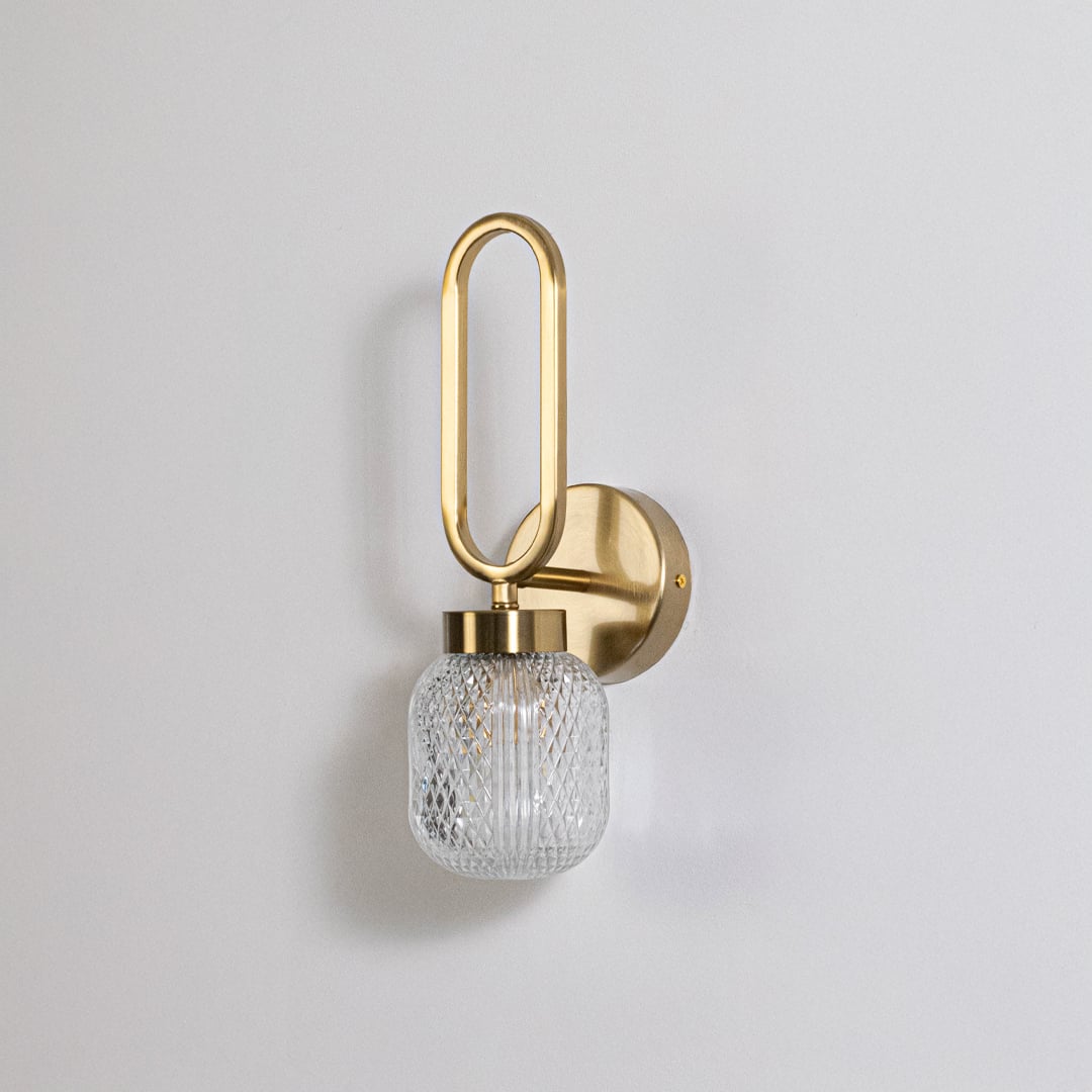 Minimalist gold wall sconce with loop frame and textured glass shade switched off displayed on plain white background for product use.