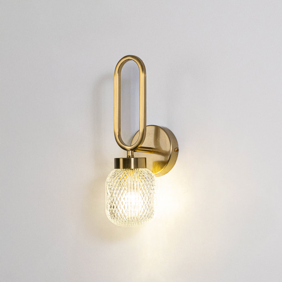 Modern wall light with gold metal frame and round glass bulb on neutral background minimal stylish lighting ideal for bedroom and living space decor.