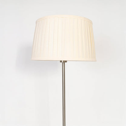 Closeup of steel floor lamp with cream pleated shade showing sleek metallic base and fine fabric detailing.