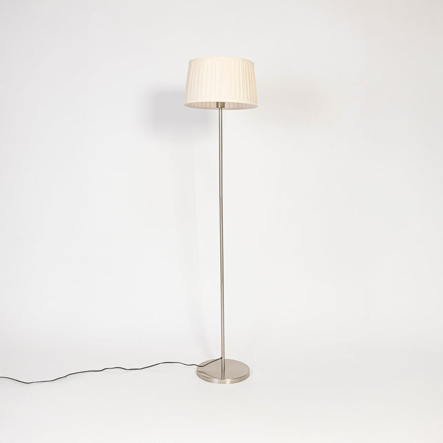 Steel floor lamp with cream pleated shade turned off on plain white background stylish decorative lighting.