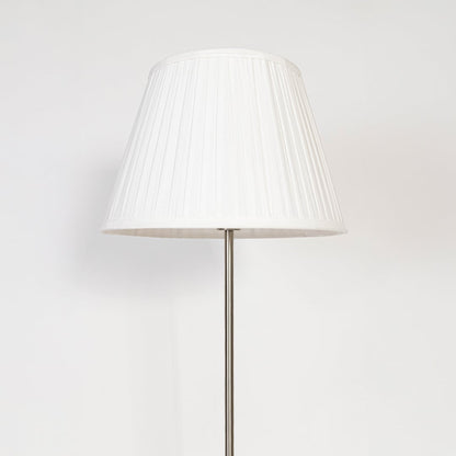 Closeup of steel floor lamp with pleated white shade showing refined modern base and fabric detailing.