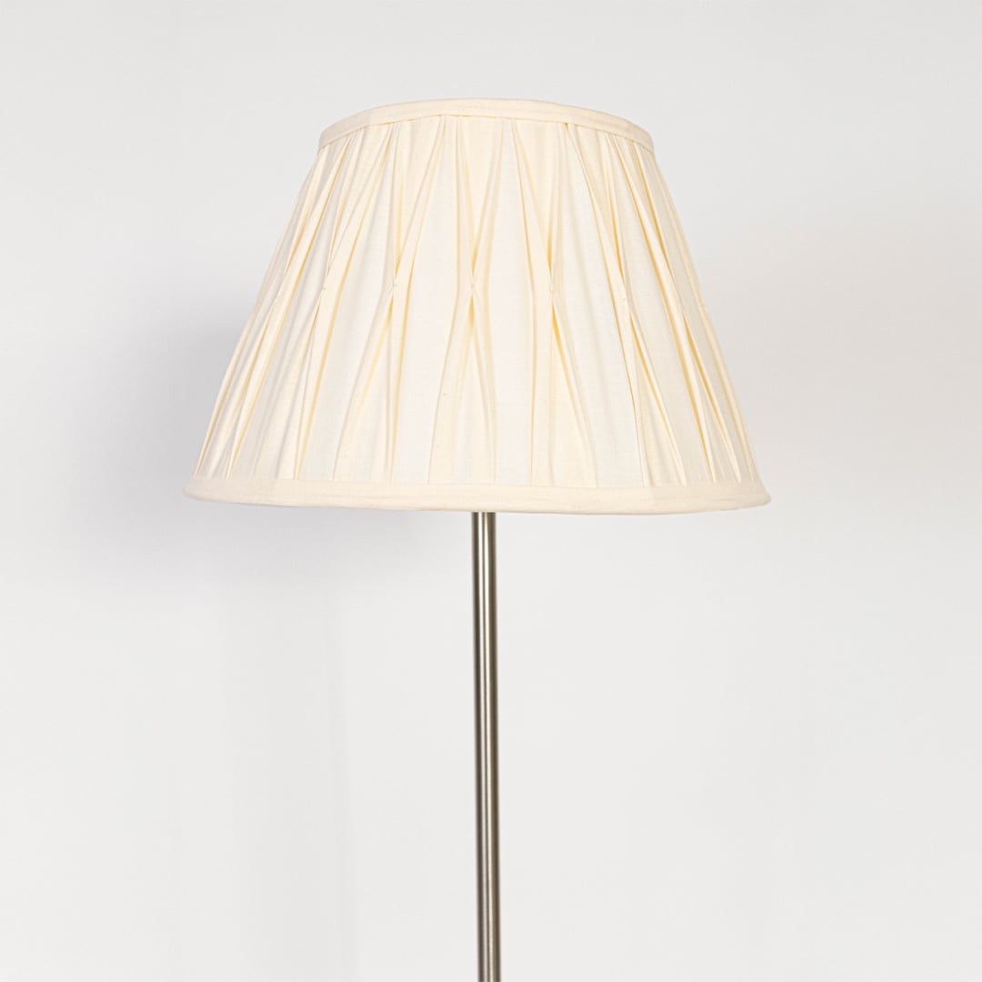 Closeup of steel floor lamp with pleated cream fabric shade showing fine detailing and sleek base design.