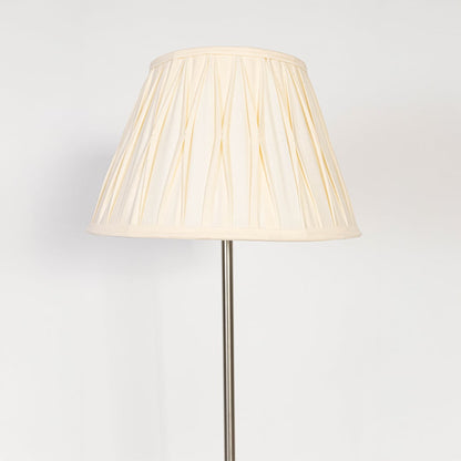 Closeup of steel floor lamp with pleated cream fabric shade showing fine detailing and sleek base design.