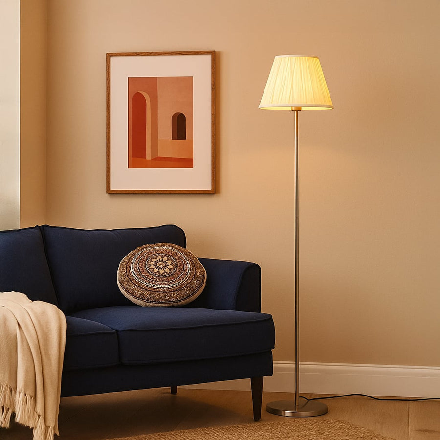 Steel floor lamp with pleated cream shade beside navy sofa and wall art in modern living room lighting decor.