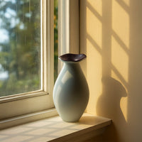 Elegant ceramic vase in soft white with curved design styled on a window sill for modern home decor.