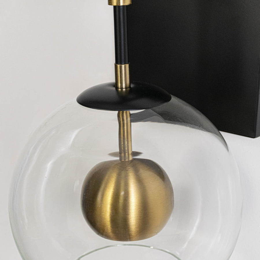 Closeup image of black metal wall light with transparent glass globe and gold accent for modern interior decor.