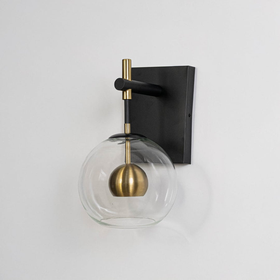 Black metal wall light on white background with clear glass globe and gold accent for stylish bedroom decor.