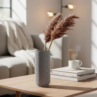 Lifestyle image of a grey grid textured ceramic vase styled with brown pampas grass on a modern living room coffee table.