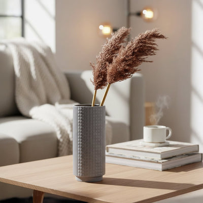 Lifestyle image of a grey grid textured ceramic vase styled with brown pampas grass on a modern living room coffee table.