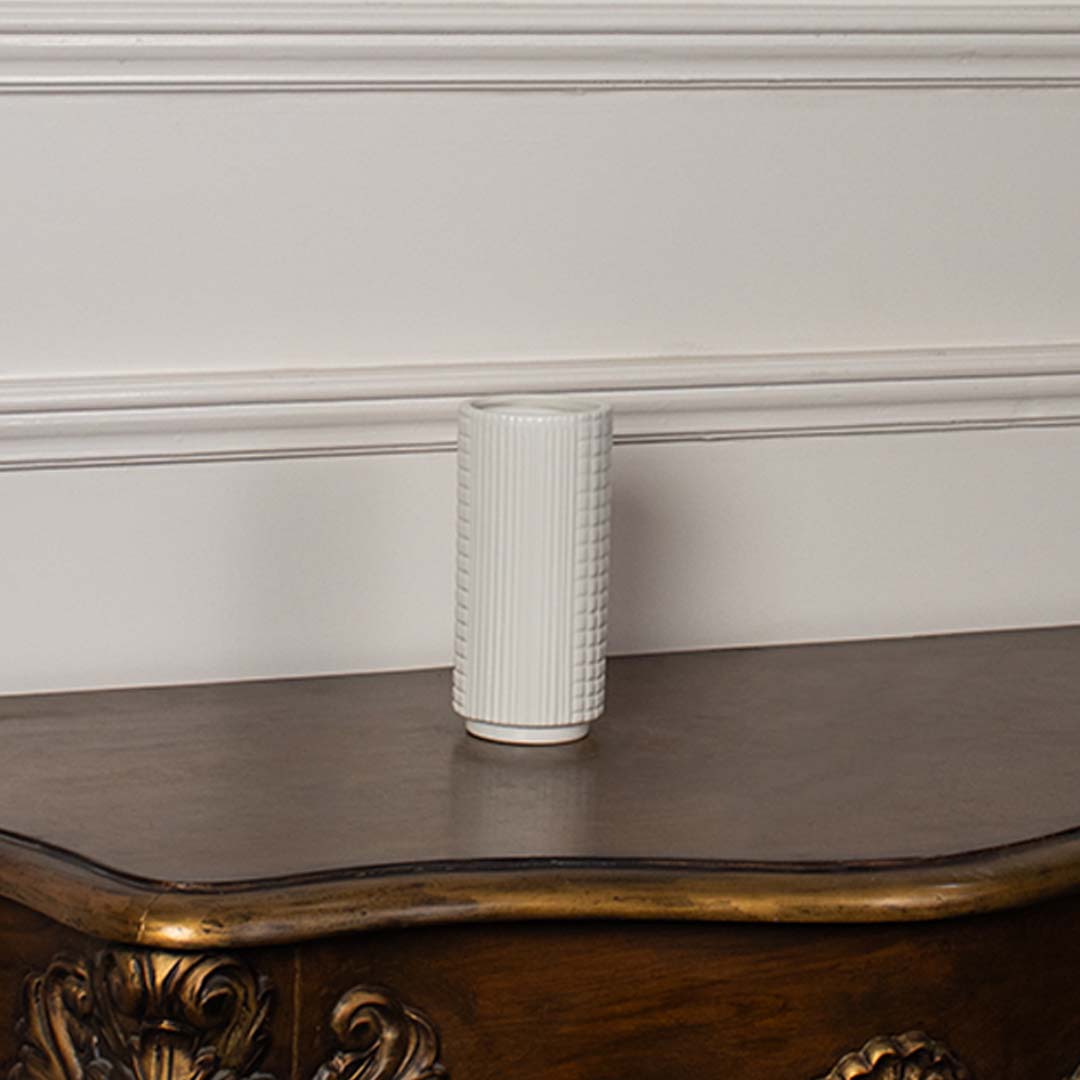 White ceramic cylindrical vase styled on a vintage wooden console table for elegant modern home decor arrangements.