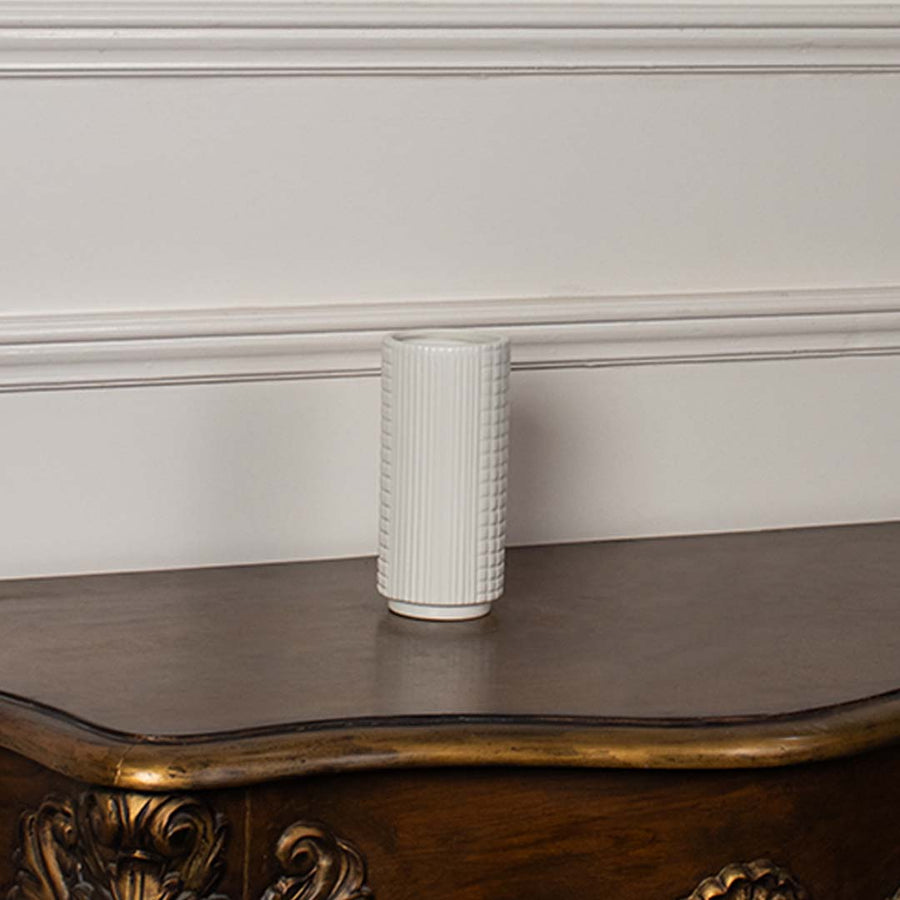 White ceramic cylindrical vase styled on a vintage wooden console table for elegant modern home decor arrangements.