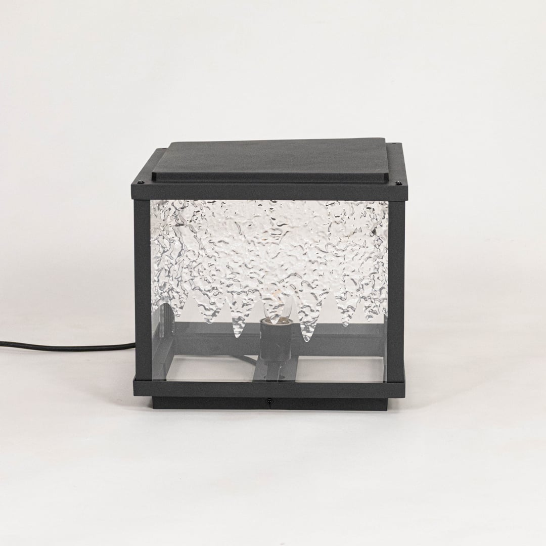 Sleek pillar light with black metal frame and textured clear glass displayed off on plain white background.