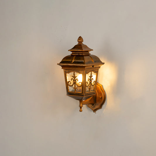 Antique brass outdoor wall lantern on white background with clear glass panels and intricate metal overlay filigree decor.