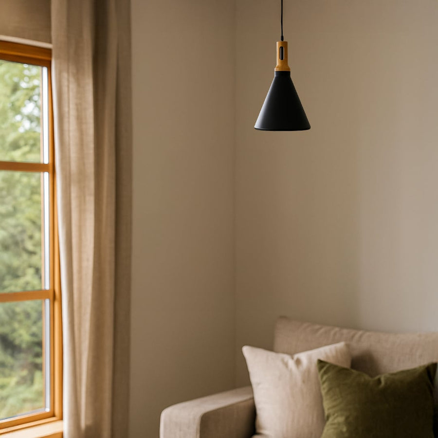 A modern black cone pendant lamp with wooden detail hanging over a cozy sofa in a warm neutral living room creating a soft ambient glow in the space.