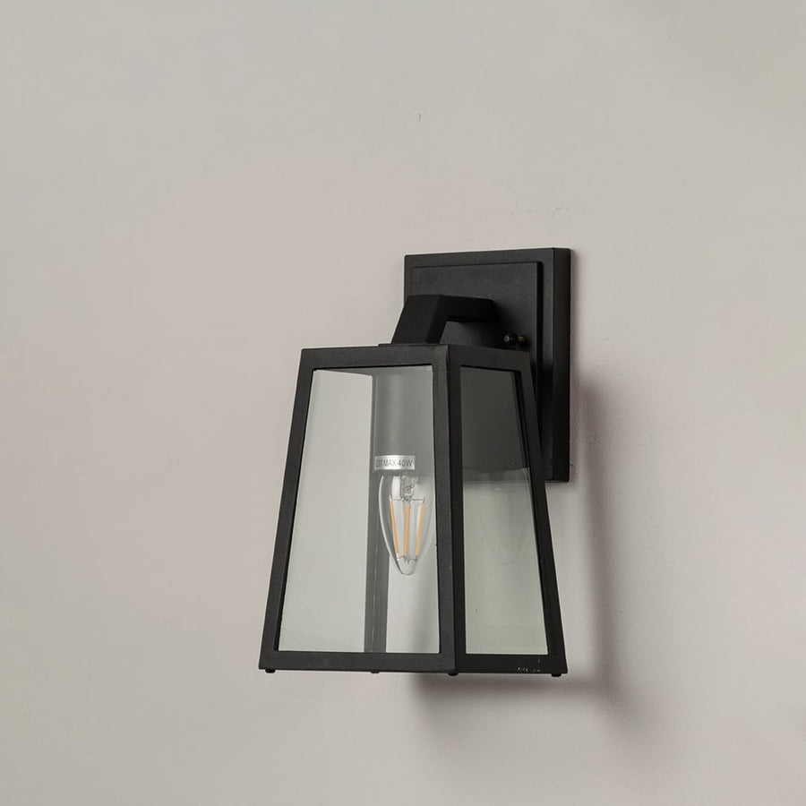 Black metal outdoor wall lantern with geometric frame and clear glass panels displayed on white background for product detailing.