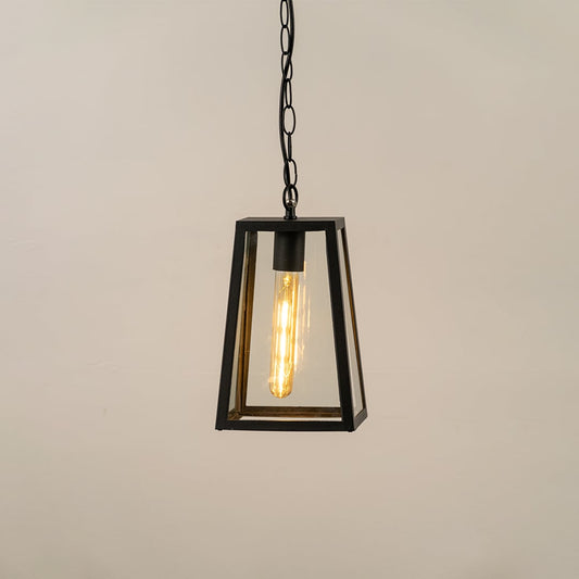 Black modern hanging lantern on white background with light on showing warm glowing filament inside clear tapered glass panels perfect for outdoor ceiling lighting.