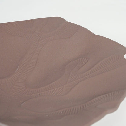 Close view of brown ceramic platter showcasing embossed artistic detailing and smooth matte finish.