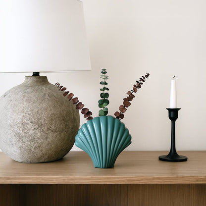 Teal ceramic shell shaped vase styled on a clean surface adding a modern coastal touch to home decor with its smooth glossy finish.
