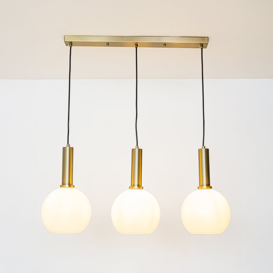 Gold and white glass pendant lights glowing softly on a white background creating warm ambient illumination.