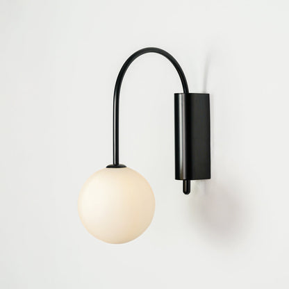 Contemporary wall sconce with curved black arm and frosted glass globe mounted on neutral wall background ideal for bedroom lighting.