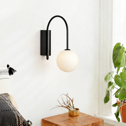 Modern wall light with black metal arm and white glass globe installed beside wooden table in cozy living room setting.