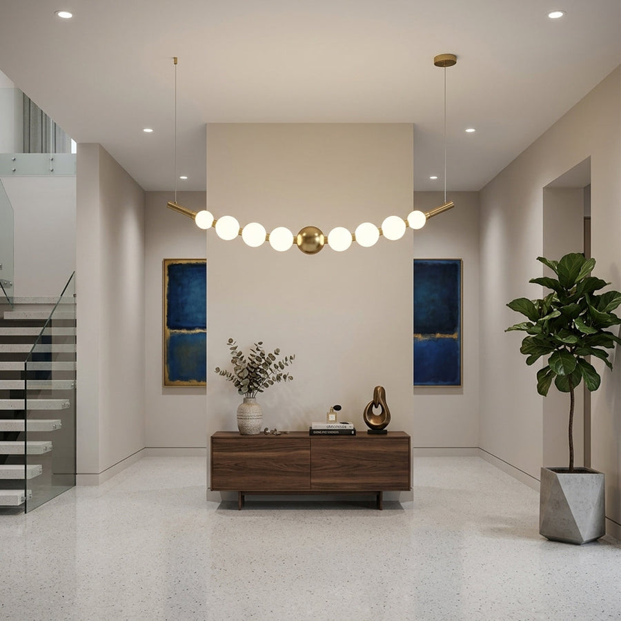 Modern linear pendant light with white glass globes and gold metal accents installed above wooden console in spacious living room interior.