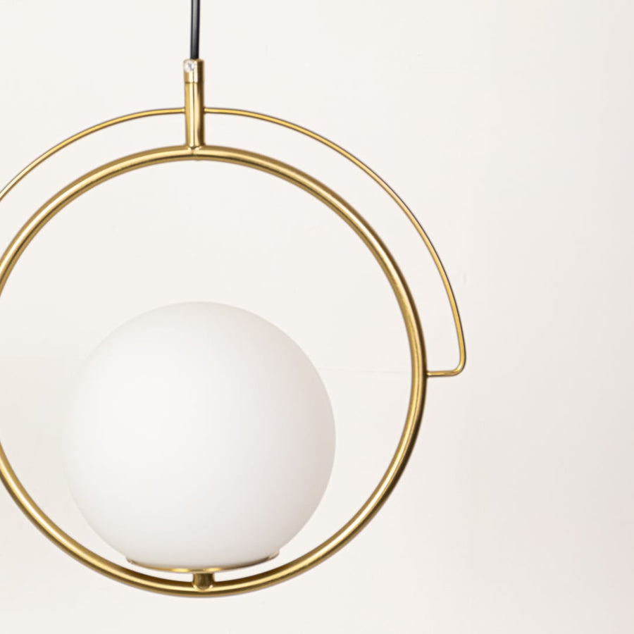 A closeup view of the gold circular pendant light highlighting the smooth white globe and metal frame with detailed texture visible in soft lighting.