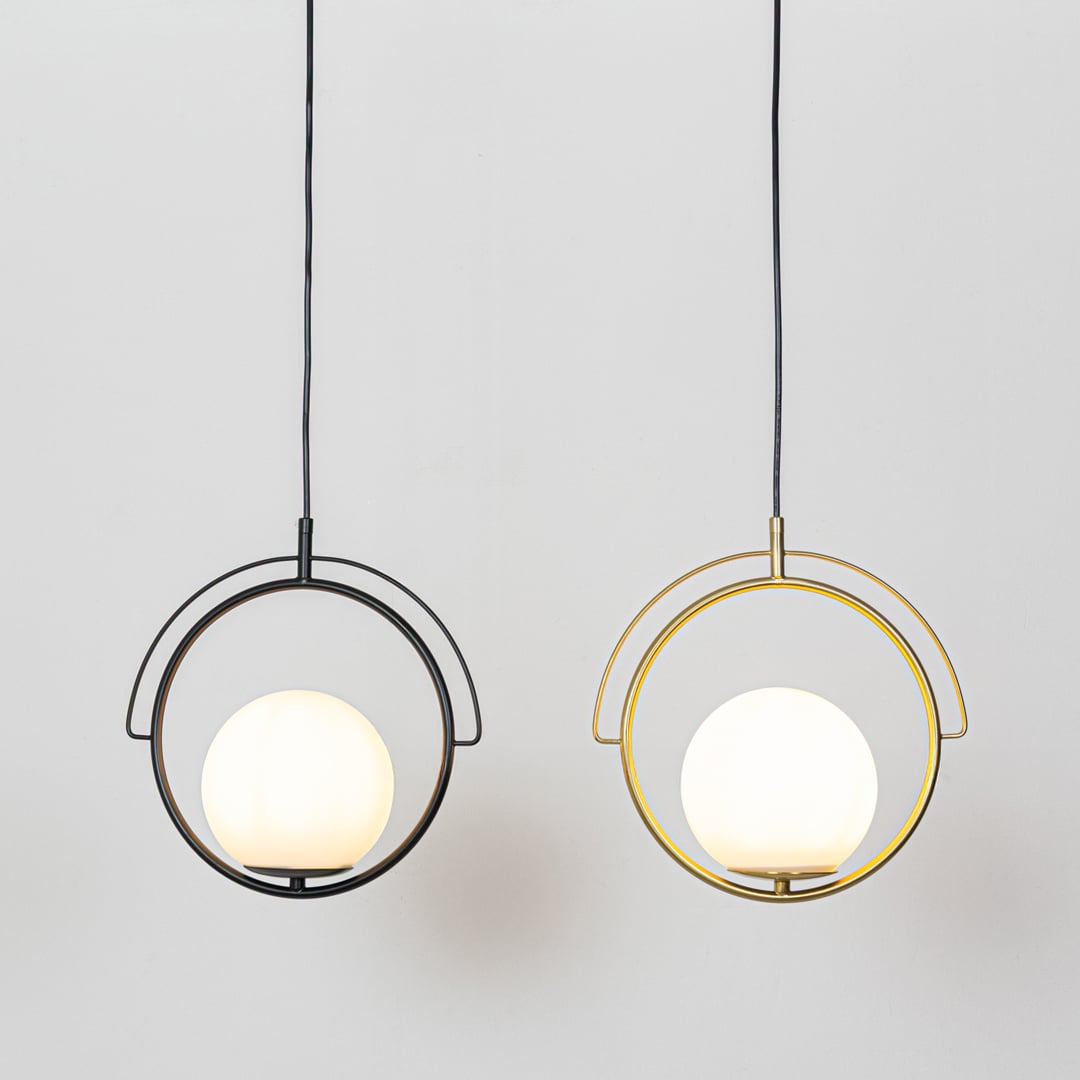 A gold circular pendant light with a white globe shade hanging against a plain background showing warm light glowing from the central globe when switched on.