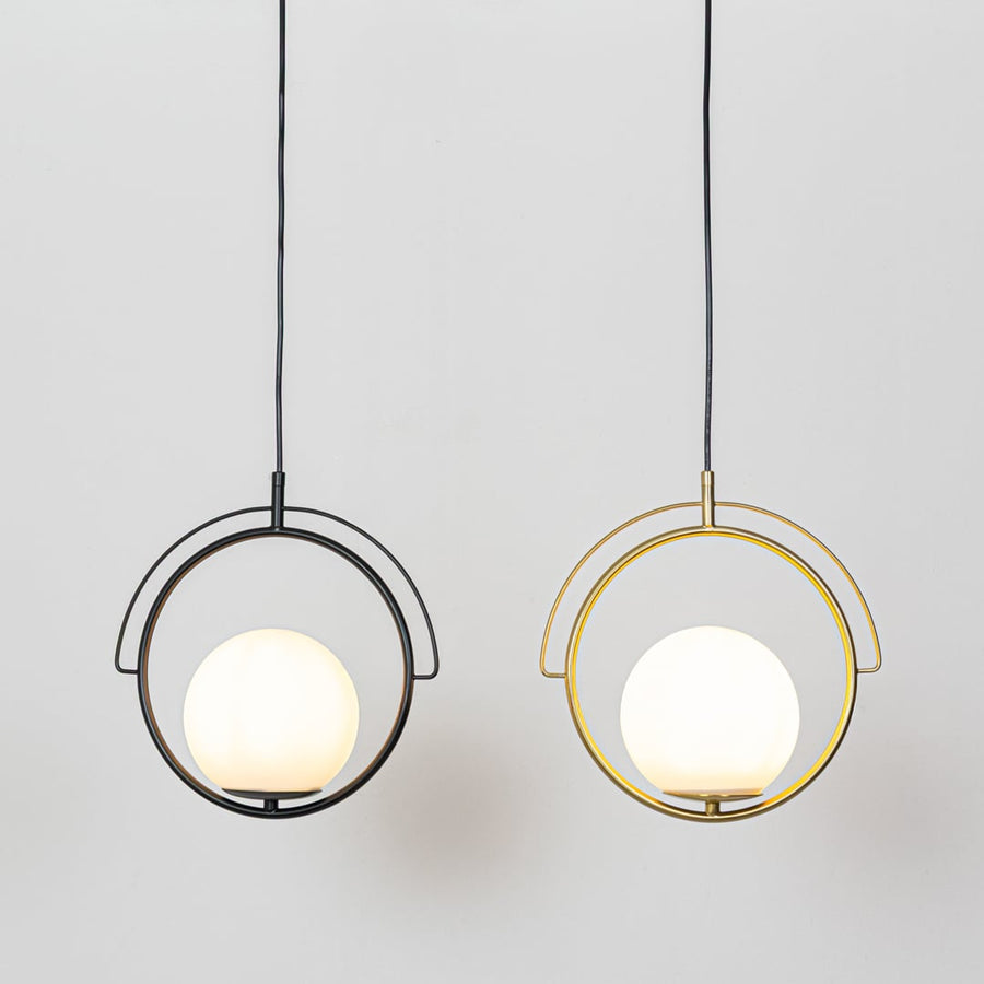 A gold circular pendant light with a white globe shade hanging against a plain background showing warm light glowing from the central globe when switched on.