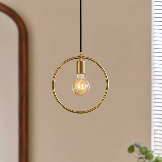 A round brass hanging light with a warm glowing bulb displayed in a calm seating corner with a woven chair soft throw and indoor plant creating a cozy look.