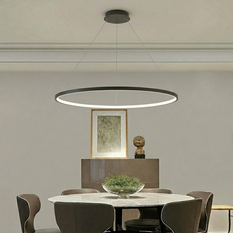 Minimal circular ring pendant light with soft glow suspended above dining table in modern interior setting with neutral wall background.
