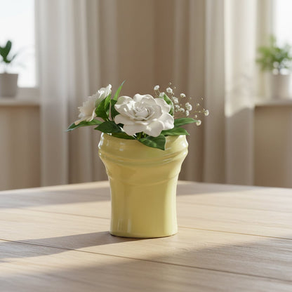 Soft yellow ceramic decorative vase styled with white floral arrangement on wooden table in bright cozy living room.