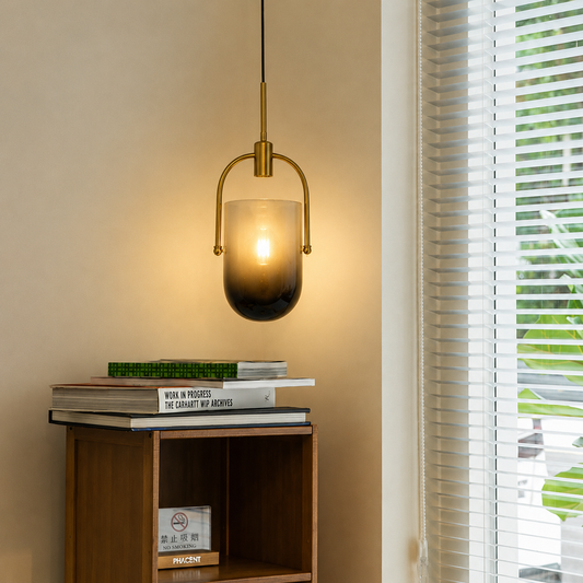 Modern brass arch frosted smoke glass capsule pendant light hanging next to a window with blinds above a wooden shelf unit.