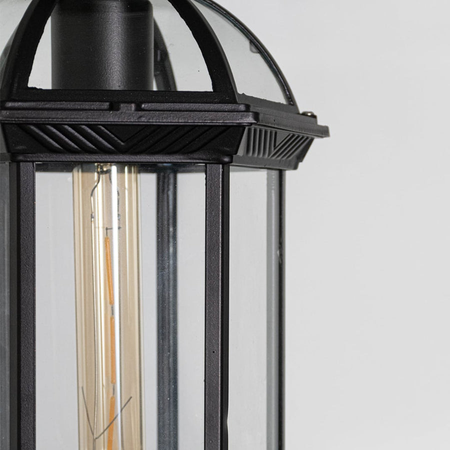 Closeup of black outdoor wall lantern with clear glass panels vertical frame and visible filament bulb classic exterior design.