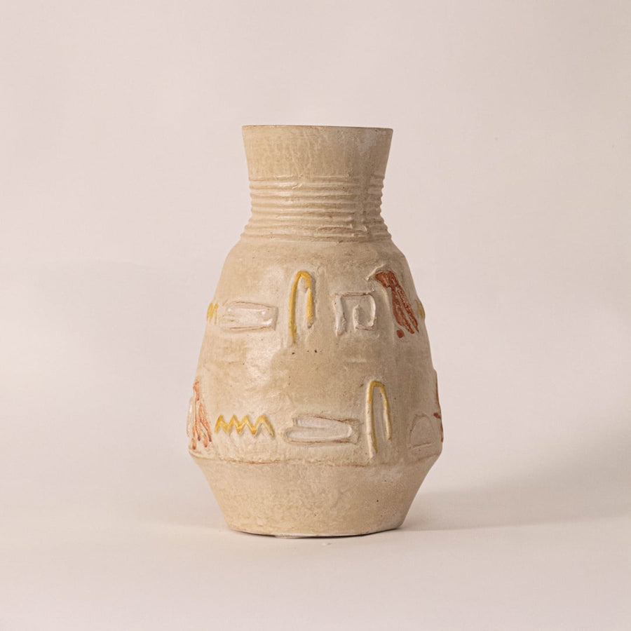 Small hieroglyph vase on off-white background under soft light emphasizing its rustic hand-carved patterns.