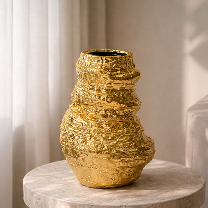 Gold textured metal floor vase with sculpted form styled beside sofa for luxury living room decor accent.