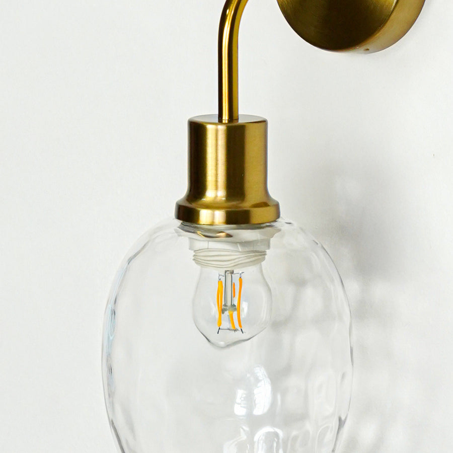 Closeup of gold metal wall light with clear textured glass shade for luxury modern interior decor styling.