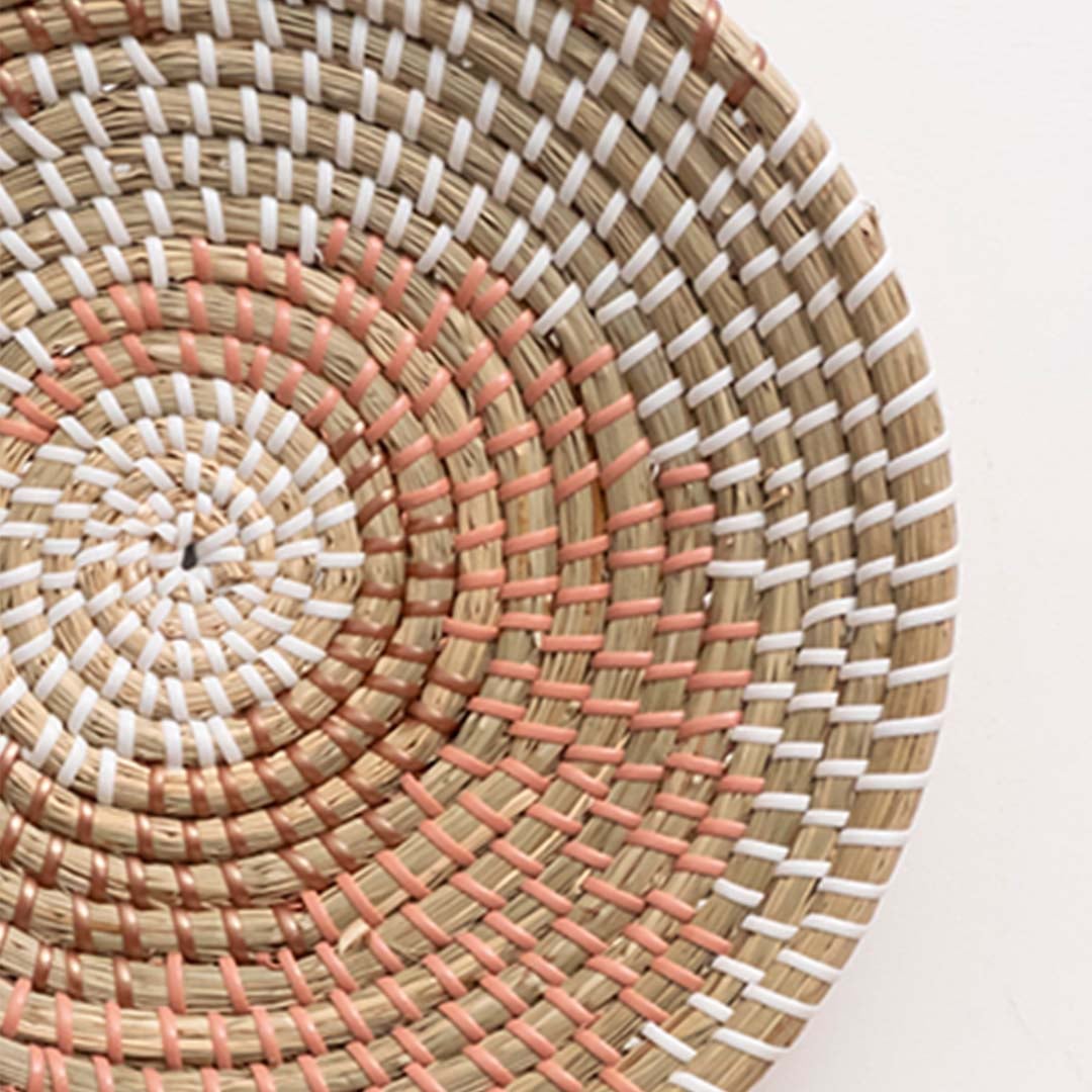 Closeup of handwoven wall basket in natural fiber with pink and white woven detailing for boho wall decor.