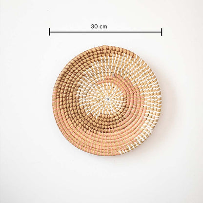 Handwoven wall basket decor in natural and pink fiber shown with 30cm diameter for decorative wall use.