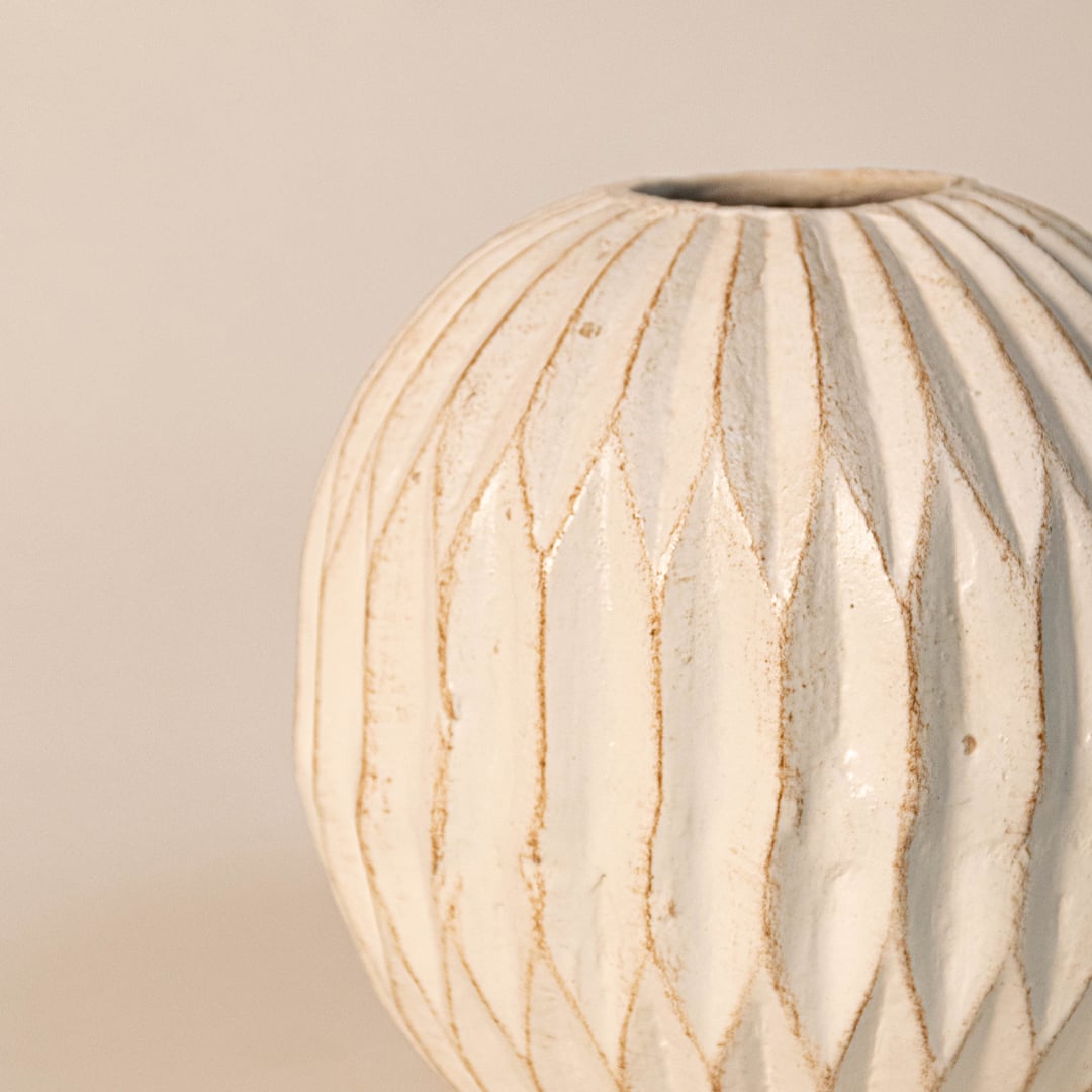 Close up of round carved vase showing detailed geometric carvings and hand-textured ceramic artistry.