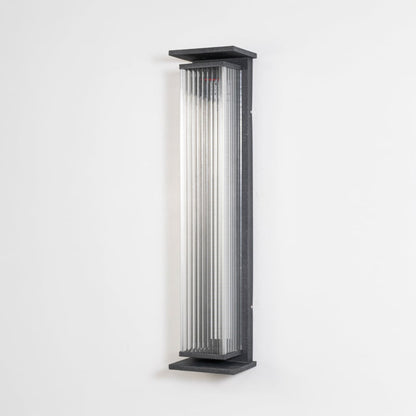 Black ribbed wall light with vertical glass shade displayed off on plain white background surface.