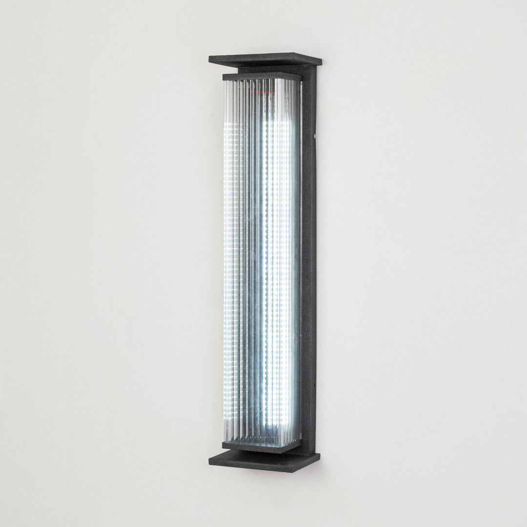 Black metal outdoor wall light on white background with ribbed glass shade for modern exterior decor.